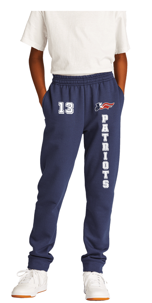 Youth-sized fleece jogger pants in blue with a self-fabric waistband and cuffs, featuring a logo on the left leg. The jogger is paired with a white t-shirt and white sneakers.