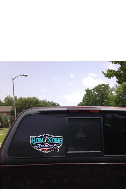Truck window with a 'Ron and Sons Towing' decal against a clear sky and trees background. Paper Street Print Co, Blairstown, NJ.