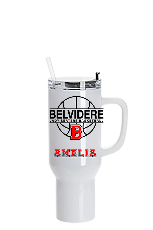 A white insulated travel tumbler with a handle, clear lid, and straw. The front features a black basketball graphic with the text 'BELVIDERE LADY SEATERS BASKETBALL', a red block 'B', and the name 'AMELIA' in red. Paper Street Print Co, Blairstown, NJ.