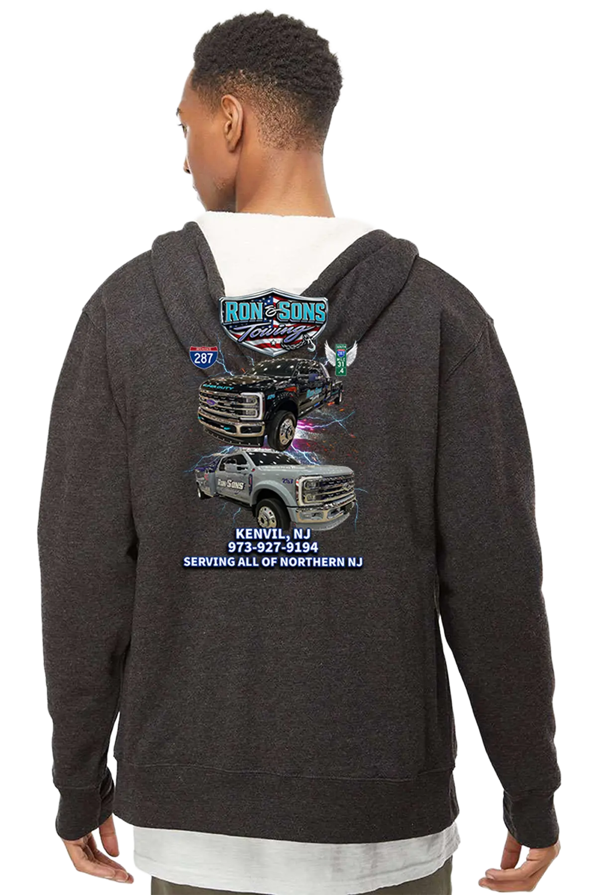 Person wearing a dark hoodie with a graphic design on the back, featuring vehicles and text. Ron and Sons Towing, Paper Street Print Co, Blairstown, NJ.