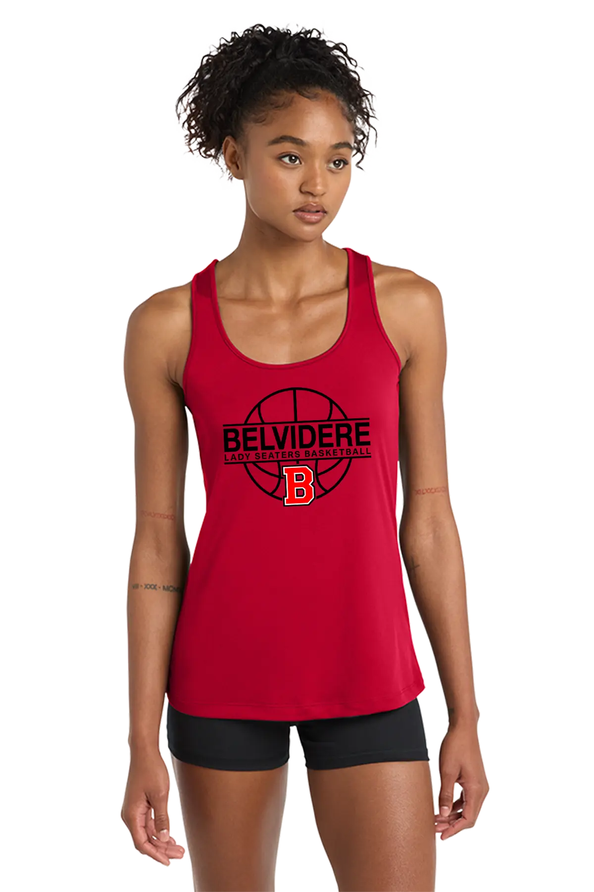 A woman modeling a red racerback tank top with a black and orange Belvidere Lady Seaters Basketball graphic on the front, paired with black athletic shorts, against a plain white background. Paper Street Print Co, Blairstown, NJ.