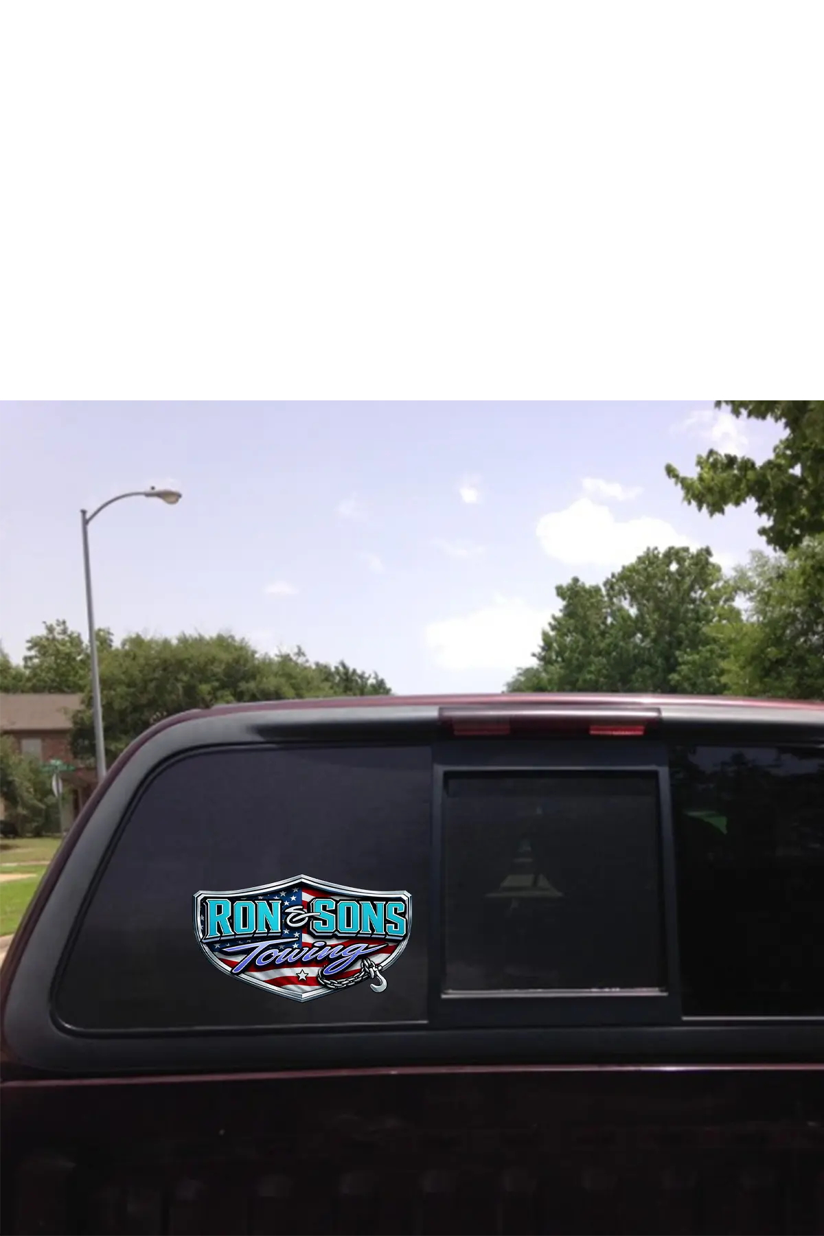 Truck window with a 'Ron and Sons Towing' decal against a clear sky and trees background. Paper Street Print Co, Blairstown, NJ.