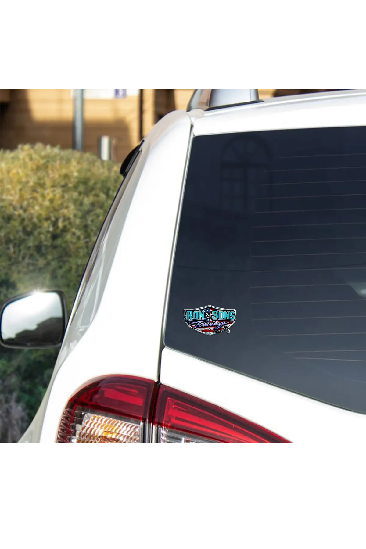 Car window with a Ron and Sons Towing decal on a white car against a blurred outdoor background. Paper Street Print Co, Blairstown, NJ.